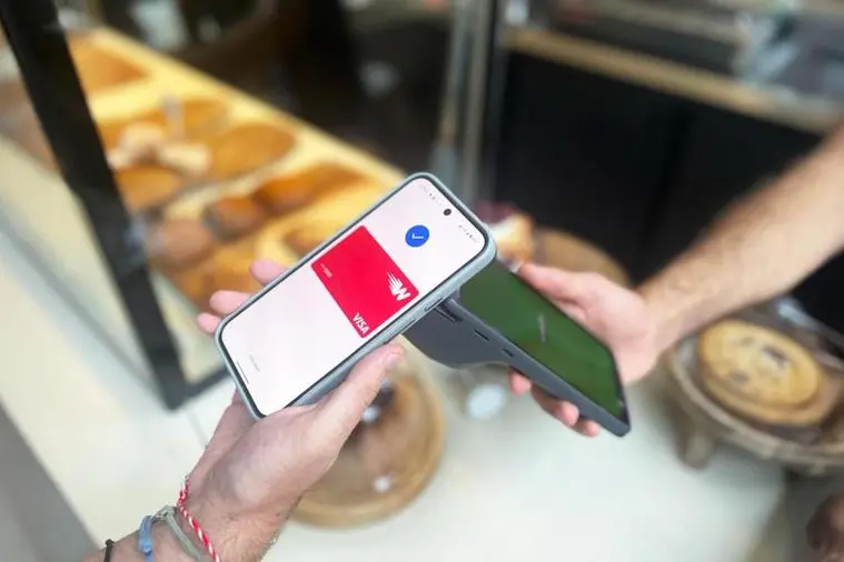 A smartphone showing a Lebanese digital wallet app in use at a Beirut shop counter, with a handwritten cash-and-wallet payment sign in the background