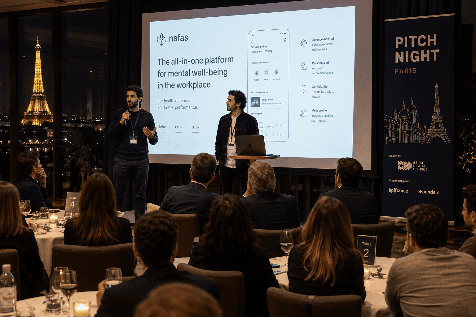Lebanese founders presenting to a room of investors at an evening Pitch Night event in Paris, with a slide deck on screen and audience seated at round tables.