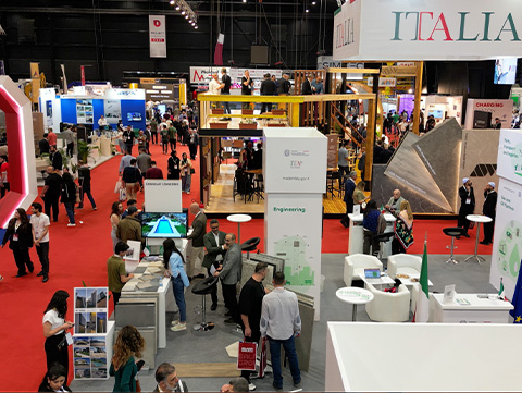 27th edition Project Lebanon trade show floor at Seaside Arena on the Beirut New Waterfront, with construction, infrastructure, electricity and renewable energy company booths and visitors walking between exhibits.