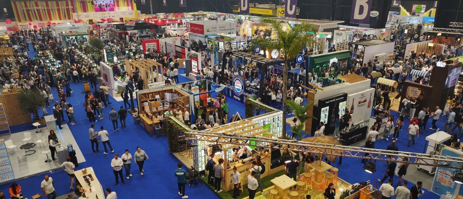 Wide shot of the HORECA Lebanon exhibition floor at Beirut's Seaside Arena, with professional visitors browsing food, beverage and equipment stands under bright overhead lighting.