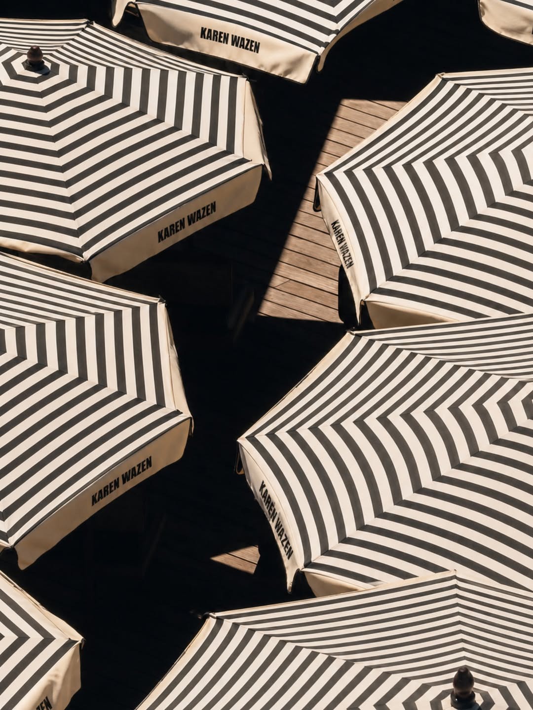 Rooftop beach club setup with black-and-cream striped umbrellas, loungers and sculptural surfboards overlooking the sea