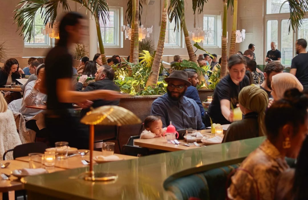 The dining room at Kalaya in Philadelphia, with tall indoor plants, wooden tables and warm lighting, co-owned by Lebanese entrepreneur Roland Kassis