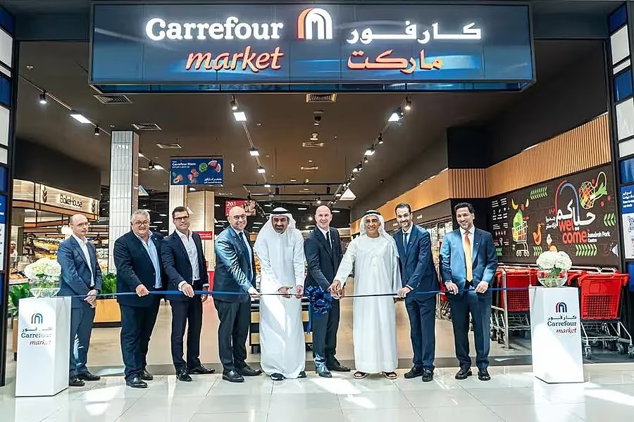Executives from Majid Al Futtaim and Dubai Holding cut a blue ribbon at the entrance of the new premium Carrefour Market in Jumeirah Park, Dubai, under the Carrefour Market sign in English and Arabic.