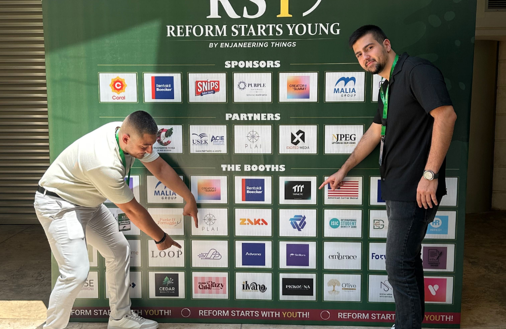 Guardify's two co-founders at the Reform Starts Young (RS19) startup event in Lebanon, leaning in to point at the TapMetic logo on the event's booth board, below rows of sponsor and partner logos.