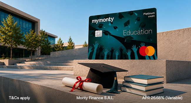 MyMonty Education Platinum Mastercard credit card in dark teal with a graduation cap illustration, standing on concrete campus steps beside a black graduation cap, a red ribboned diploma and a stack of books