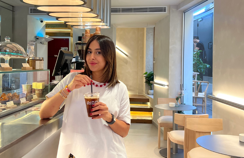 Rise founder Melissa El Haddad holding an iced coffee in a branded Rise cup at the counter of her cafe in Gemmayze, Beirut