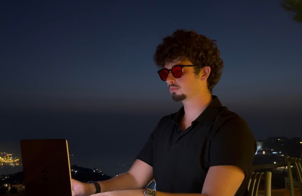Souheil Sabban, founder of Viral Vision, working on a laptop at an outdoor terrace table at night, with city lights along the coast behind him.