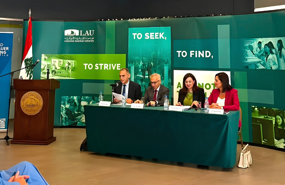 Four panelists at a table in front of a Lebanese American University backdrop, with a Lebanese flag and an LAU podium beside them, during a seminar on Lebanon's economic and political priorities.