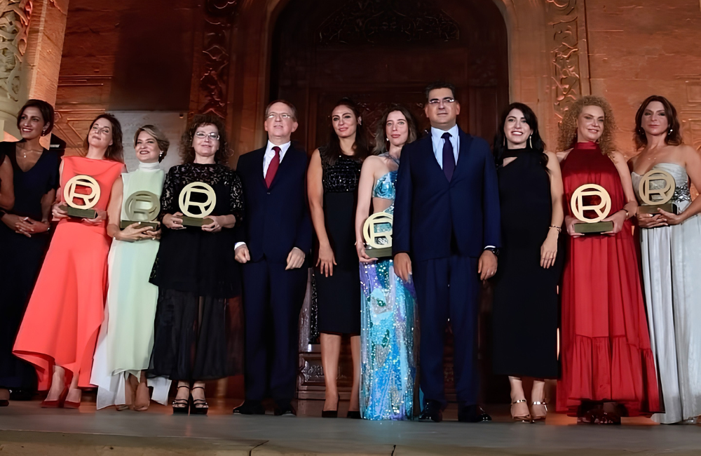 The six 2026 Women of Worth honourees hold gold trophies at the L'Oréal Paris ceremony, standing with guests in front of the stone archway of Résidence des Pins in Beirut.