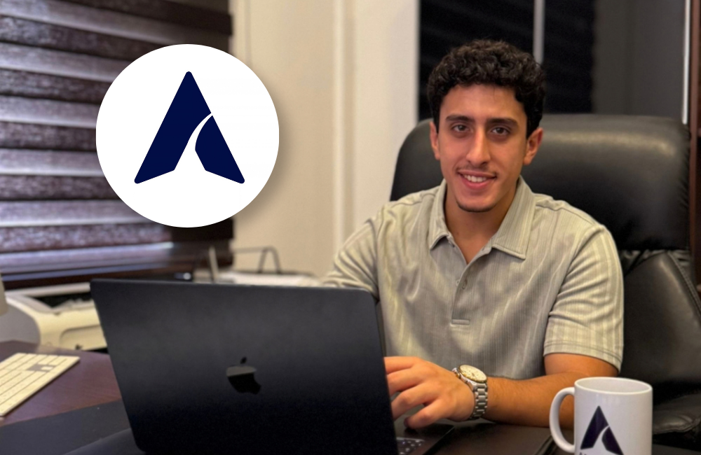 Elie Rhayem, Founder and Managing Director of Amwali Financials, smiling at his desk behind a laptop, with the Amwali Financials logo in a white circle at top left and a branded mug in the foreground.