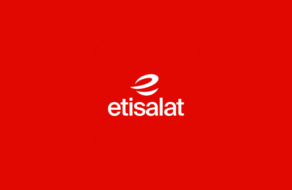 Red Etisalat sign with the new white logo outside glass office towers, with palm trees, a hedge and a bird in flight against a clear blue sky