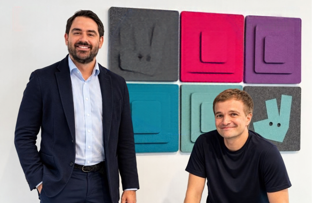 Vasilis Hadjiaslanis, Deliveroo's new General Manager for the Middle East, stands in a navy blazer next to Miki Kuusi, CEO of DoorDash International, in front of a wall of colorful felt panels with the Deliveroo kangaroo logo.