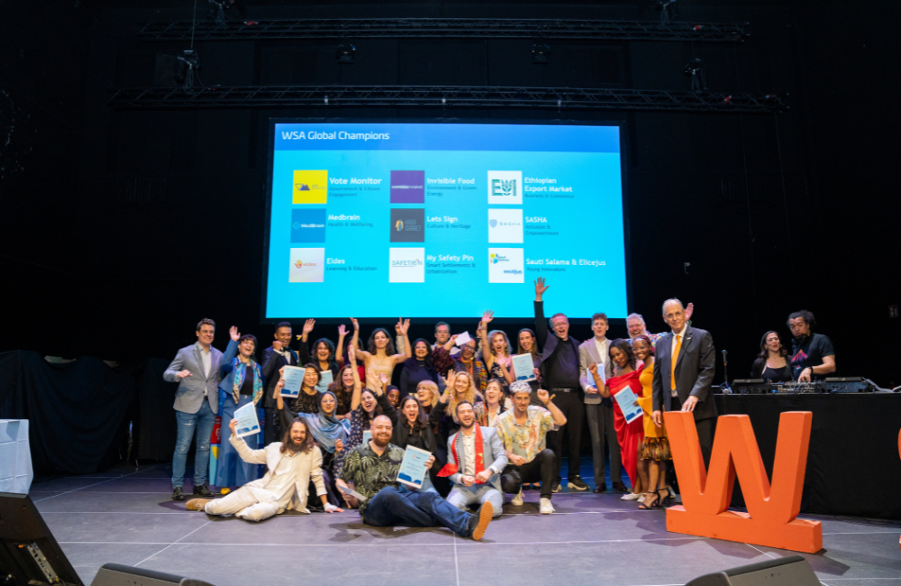 Group of WSA Global Champions celebrating on stage in front of a screen listing the winning solutions by category