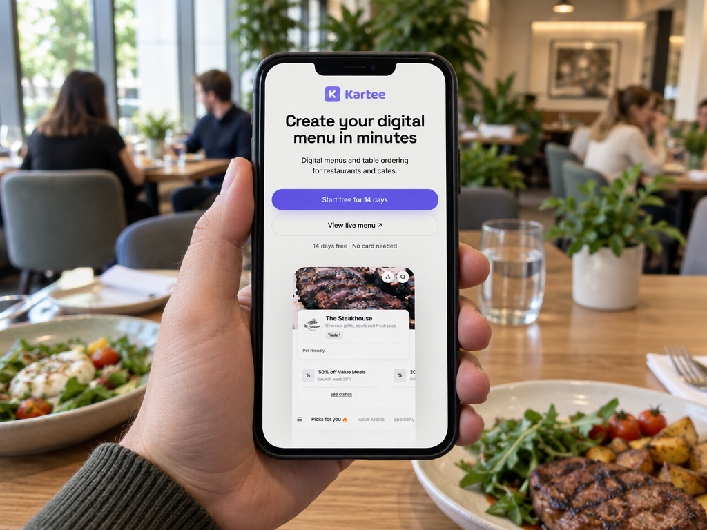 A hand holding a smartphone showing the Kartee digital menu page, with plates of salad and grilled steak on a wooden table in a bright, softly blurred restaurant.