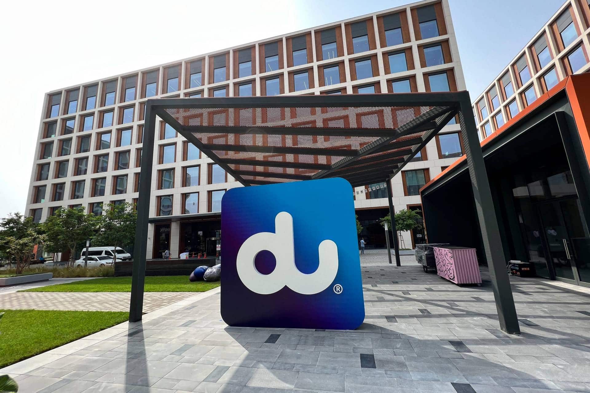 Large du logo sign under a steel canopy in front of du’s office building at Dubai Hills, with a grid of windows and landscaped grounds.