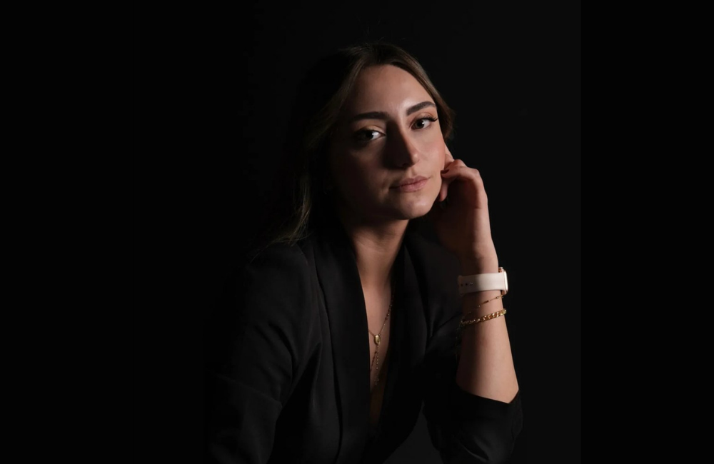 SevenPees founder and creative director Pia Takchi in a black blazer, resting her chin on her hand against a dark studio background